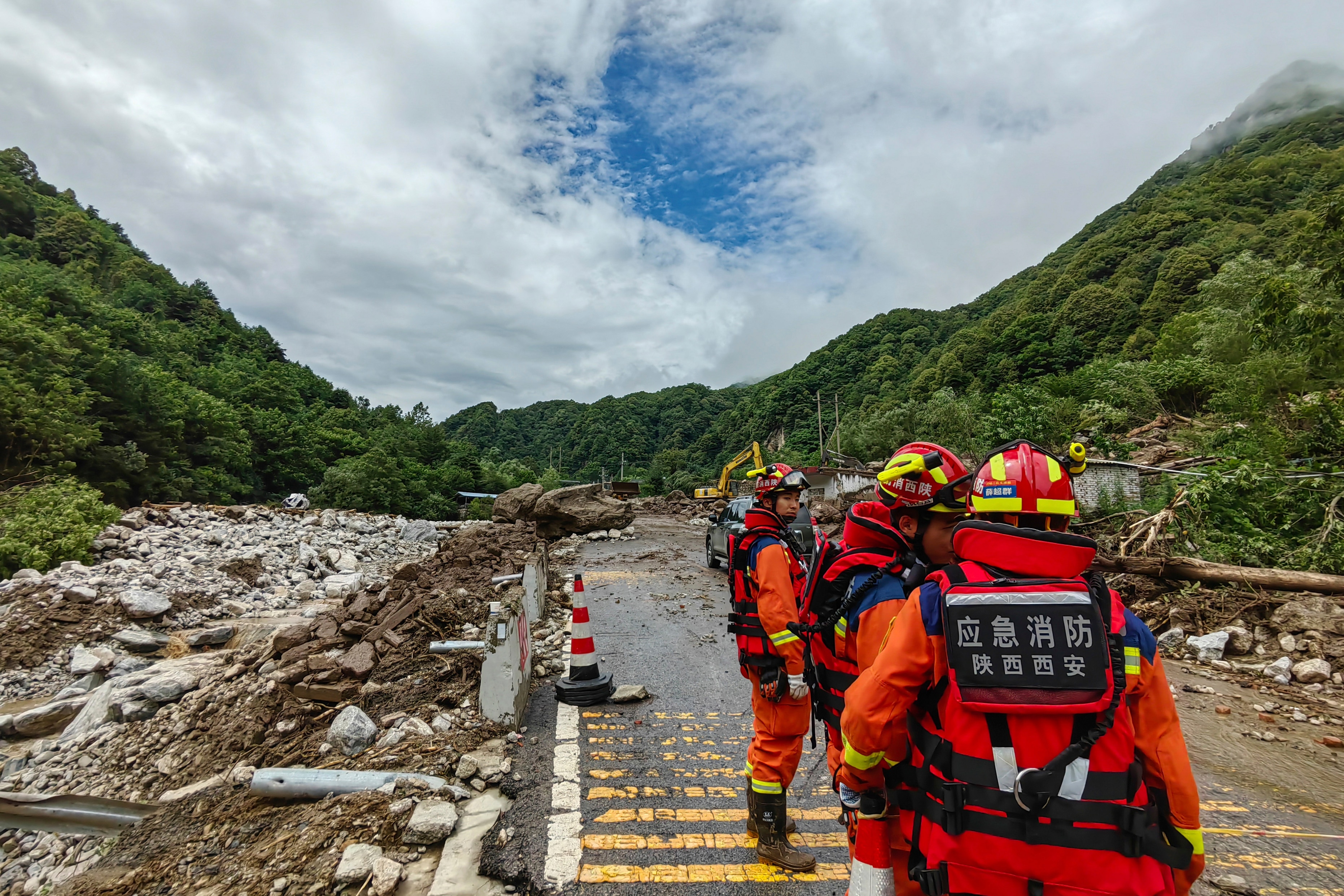 Rescue workers stand on a road surrounded by rubble from a mudslide.