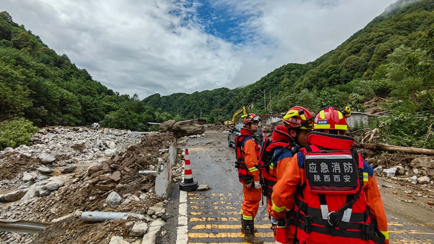 Rescue workers stand on a road surrounded by rubble from a mudslide.