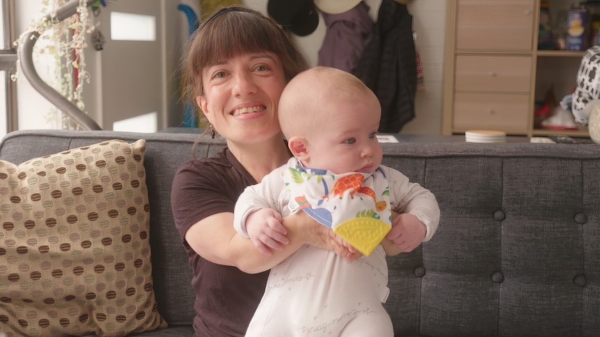 A woman holds up her baby son, who is wearing a colourful bib.