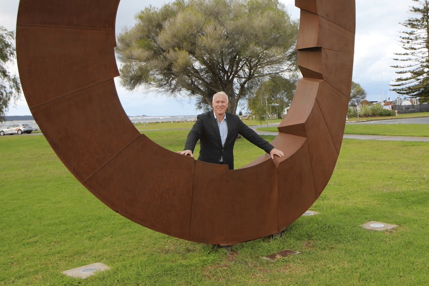 A man stands under a sculpture smiling