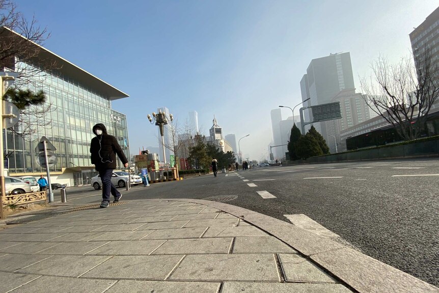 A man walks down the street wearing a face mask.