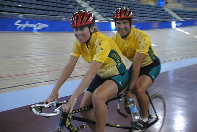 A man and women riding a tandem bike inside a veladrome.