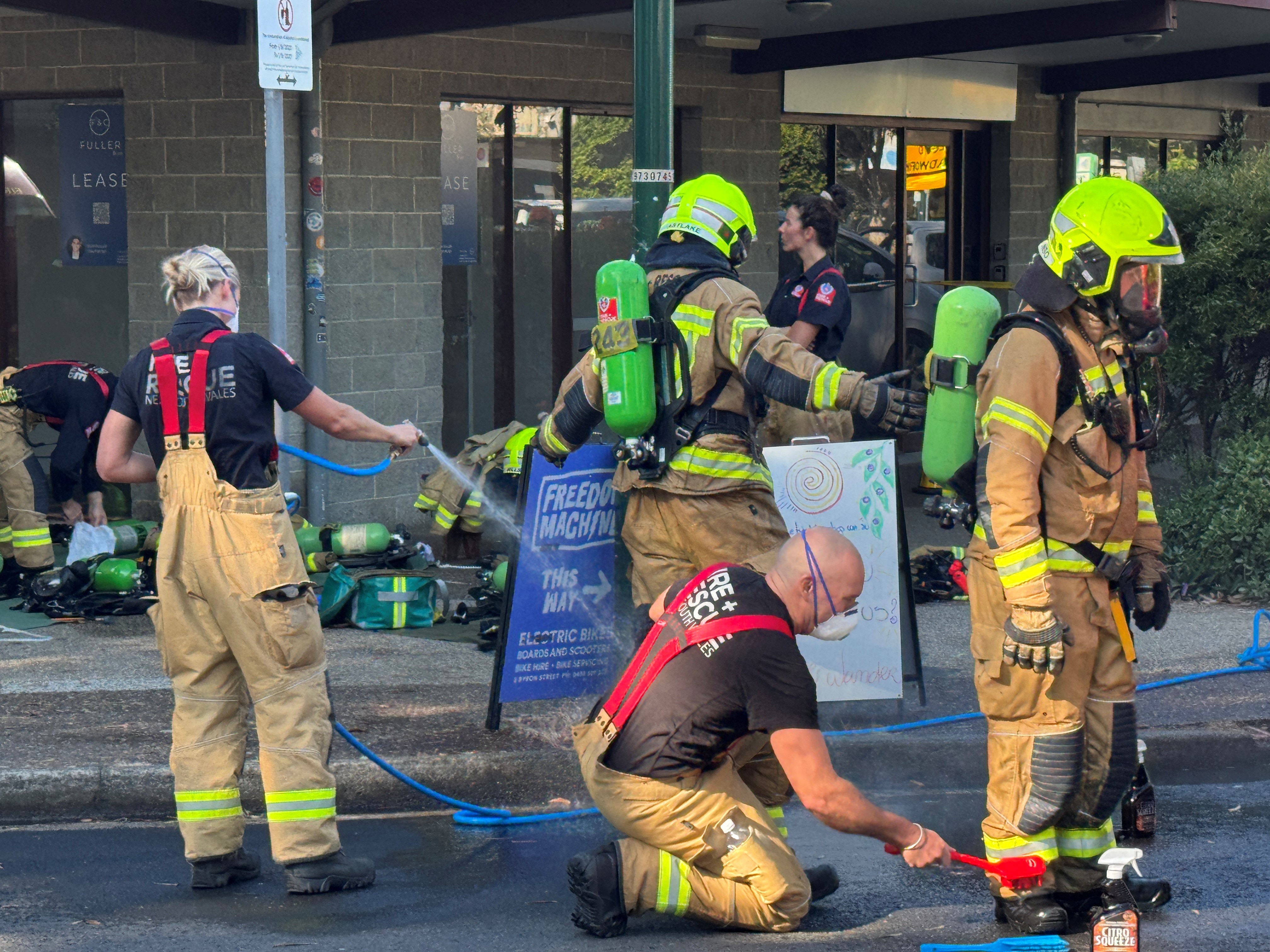 Bomberos, uno está fumigando en la calle frente a un edificio.