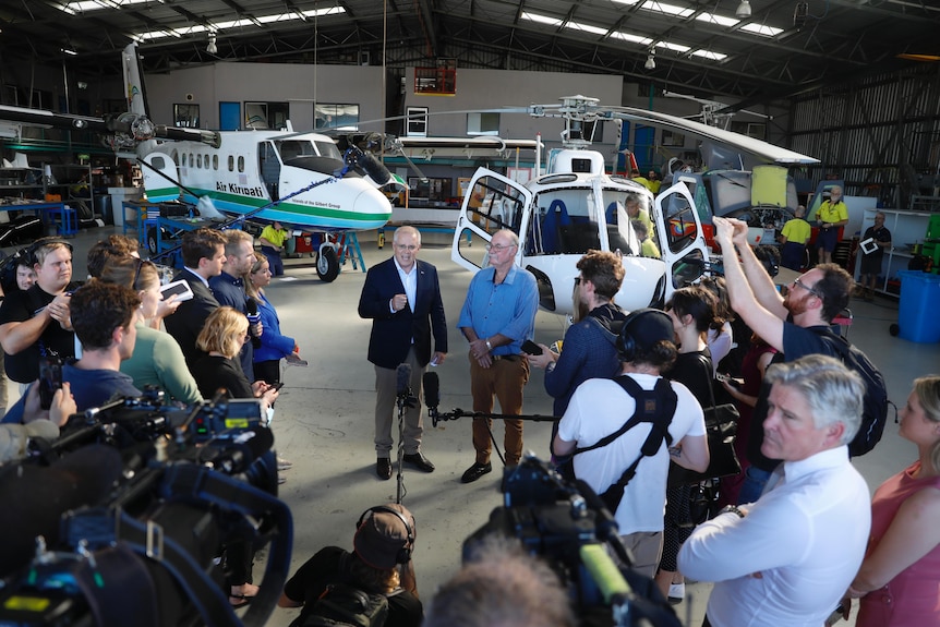 Scott Morrison speaks in an air craft hanger surrounded by media.