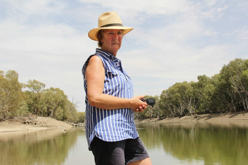 woman in hate standing in front of murky lake looking intense