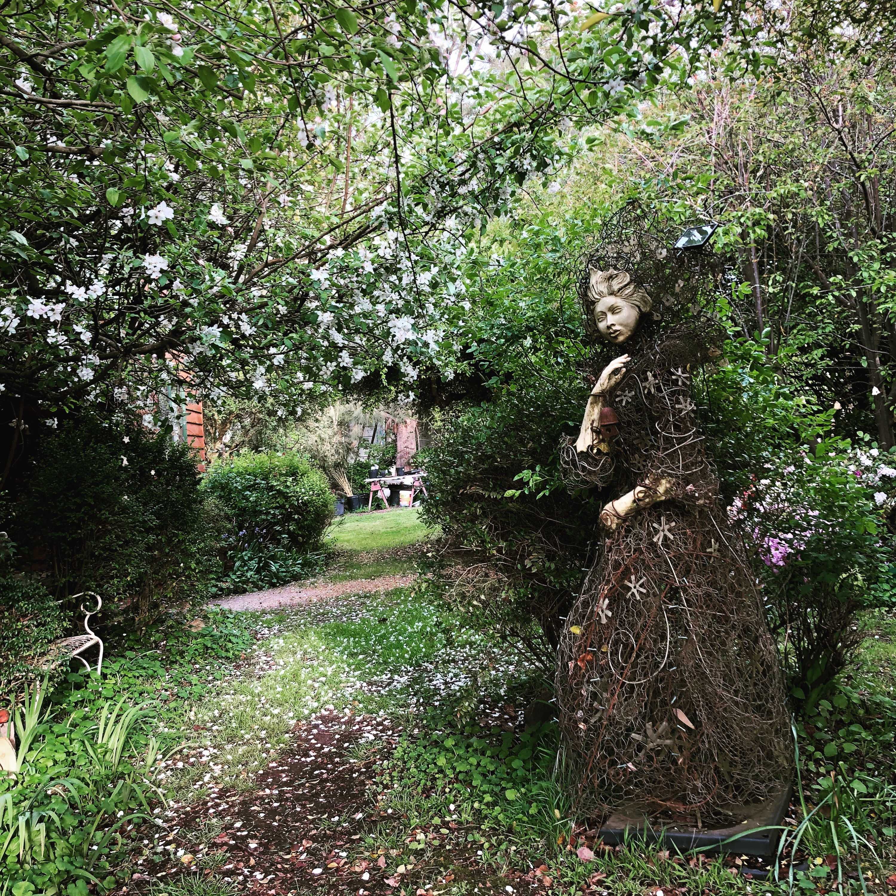 A statue made of porcelain, glass and recycled wire to look like a woman shrouded in a dress is in the garden.