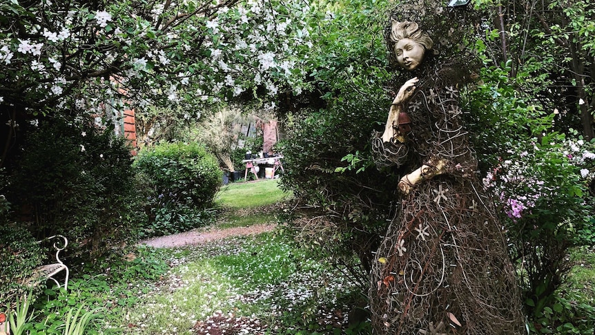 A statue made of porcelain, glass and recycled wire to look like a woman shrouded in a dress is in the garden.