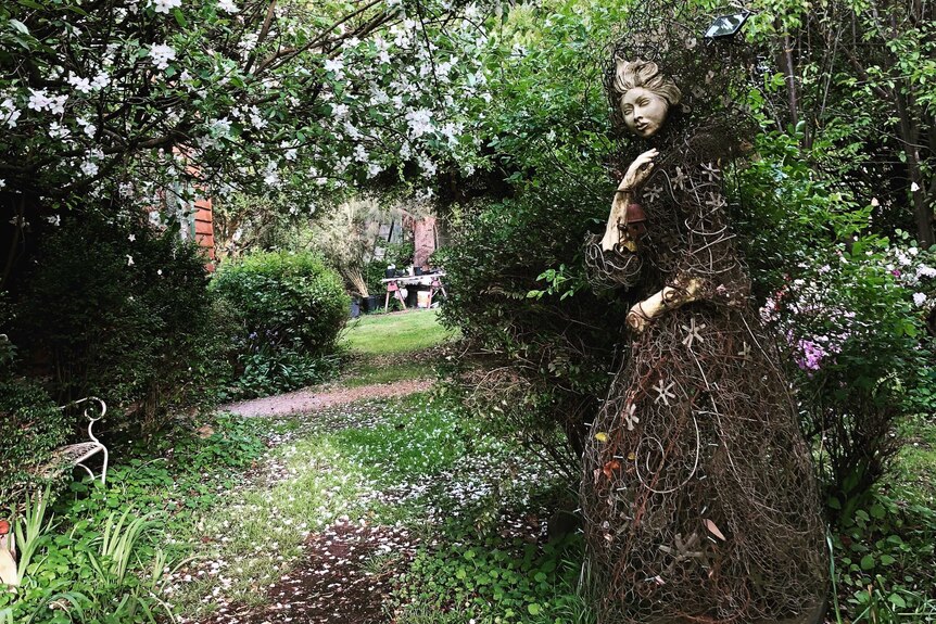 A statue made of porcelain, glass and recycled wire to look like a woman shrouded in a dress is in the garden.