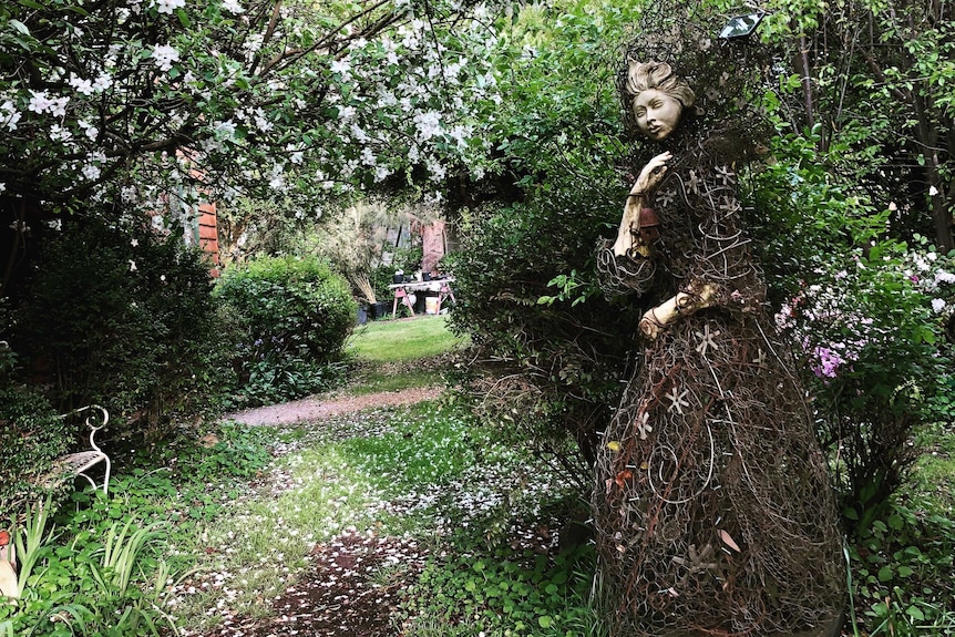 A statue made of porcelain, glass and recycled wire to look like a woman shrouded in a dress is in the garden.