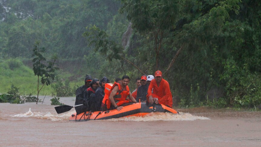 A group of people sit in an orange rubber dingy wearing life jackets.