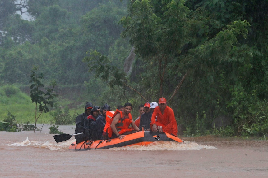 A group of people sit in an orange rubber dingy wearing life jackets.