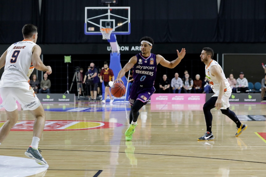 A headband-wearing NBL player runs with the ball as he looks to switch direction coming up court during a game. 