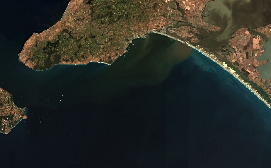 Una imagen de satélite de un tramo de costa. Se ve una nube de sedimento en el agua.