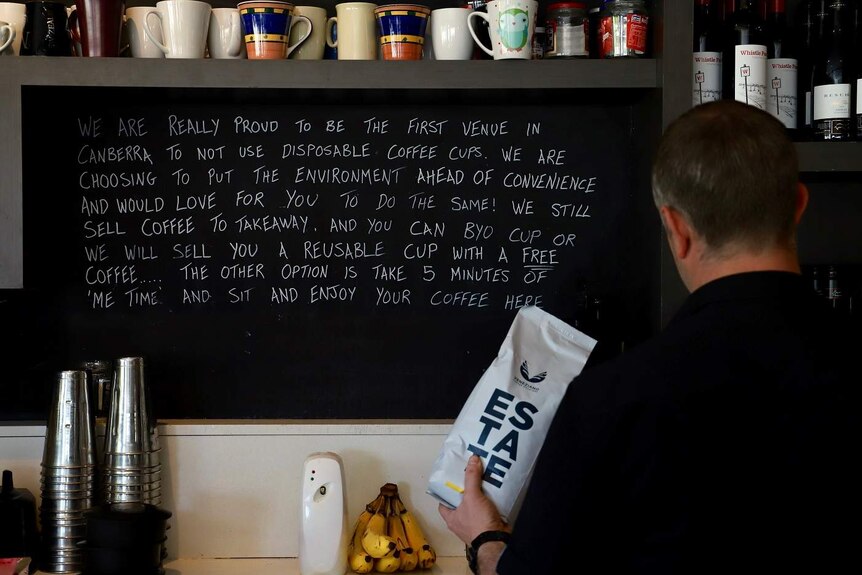 A blackboard behind the barista station, saying the cafe is proud to not use disposable cups.