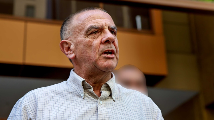 Wayne Muir speaks in front of a building.