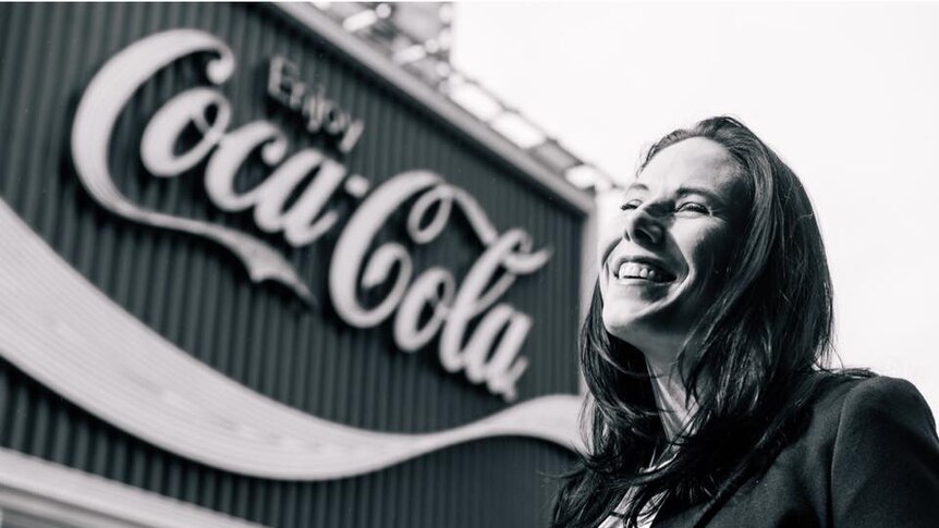 Black and white photograph of Liz Gal standing in front of Coca-Cola sign in Kings Cross, Sydney.
