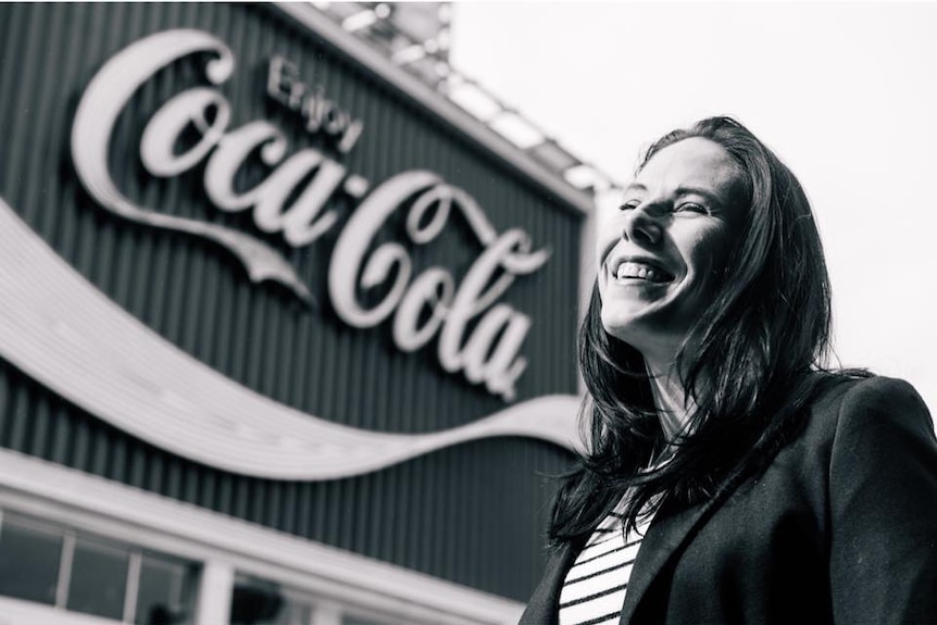 Black and white photograph of Liz Gal standing in front of Coca-Cola sign in Kings Cross, Sydney.