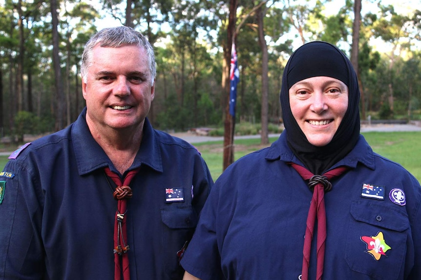 Two scout leaders in a forested parkland in front of a building