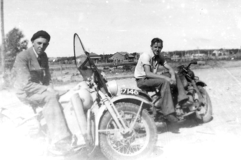Black and white photo of two young men on vintage motorbikes in deserted street