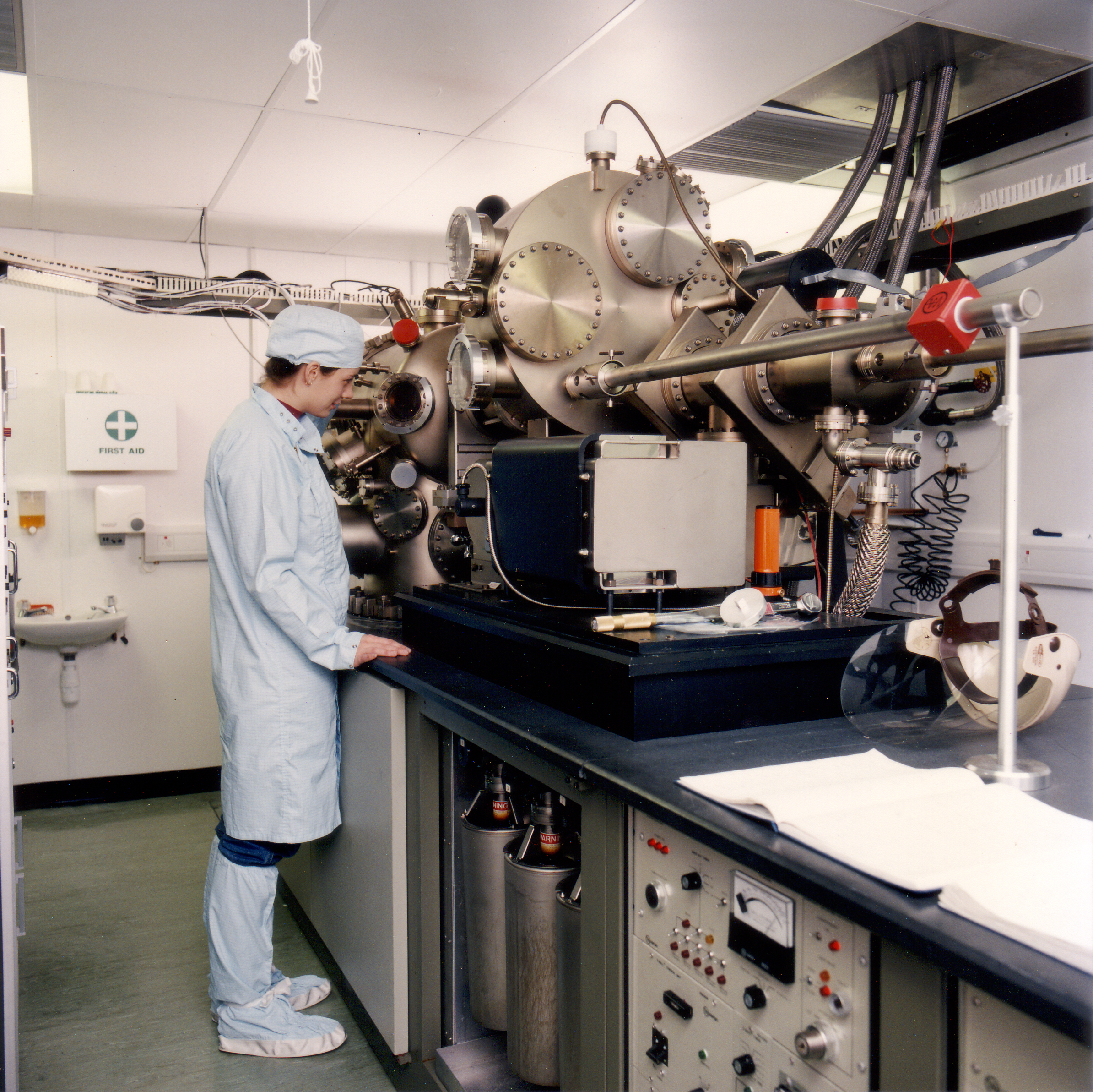 A young woman with short brown hair focuses on complex machinery in a lab.