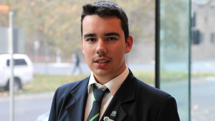 A teenage boy in school uniform looks at the camera, smiling.