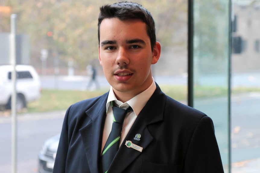 A teenage boy in school uniform looks at the camera, smiling.