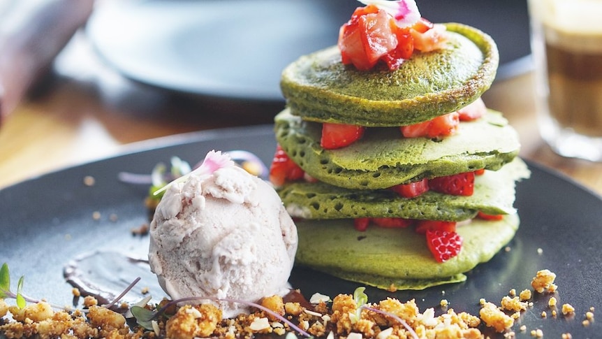 A stack of green pancakes, with chopped strawberries and a scoop of icecream.