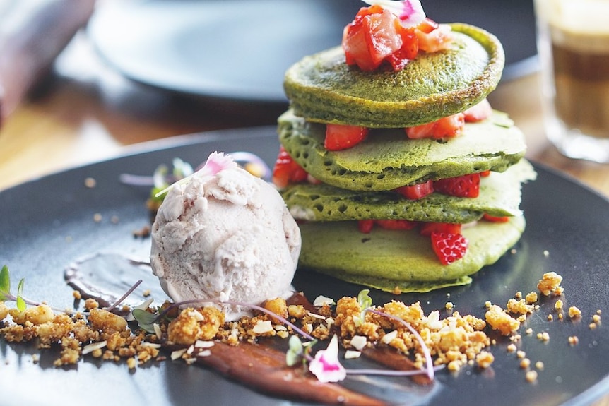 A stack of green pancakes, with chopped strawberries and a scoop of icecream.