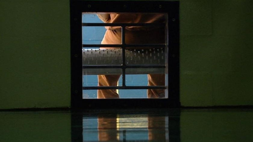 TV still of legs of a sitting anonymous prisoner, dressed in orange prison overalls, in jail (ABC TV)