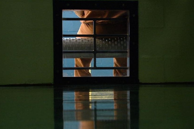 TV still of legs of a sitting anonymous prisoner, dressed in orange prison overalls, in jail (ABC TV)