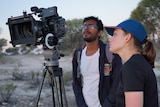 Two students look into a camera view finder while shooting a film in the Australian outback.