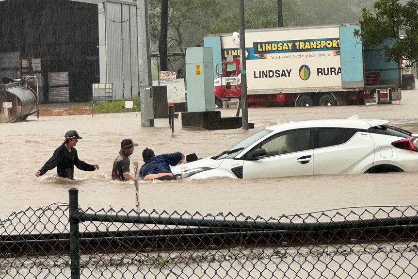 Several people walk to a submerged car.