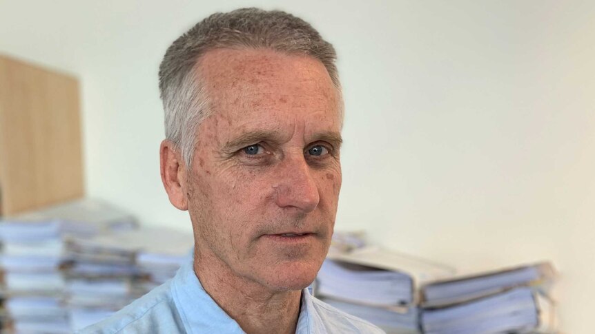 John Berrill, a lawyer stands in front of piles of paper work.