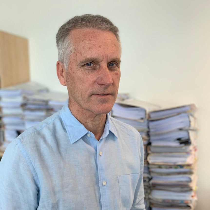John Berrill, a lawyer stands in front of piles of paper work.