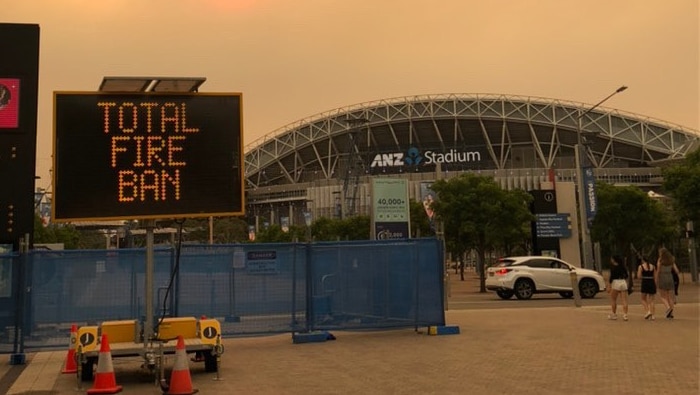 A golden sky and a digital sign reading Total Fire Ban outside a stadium