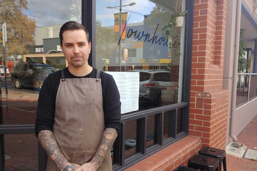 A cafe owner stands in front of his shop.