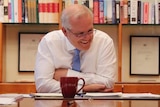 Scott Morrison sitting behind his desk with a smile on his face.