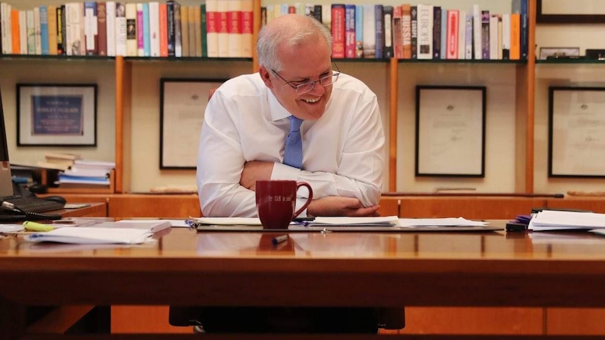 Scott Morrison sitting behind his desk with a smile on his face.