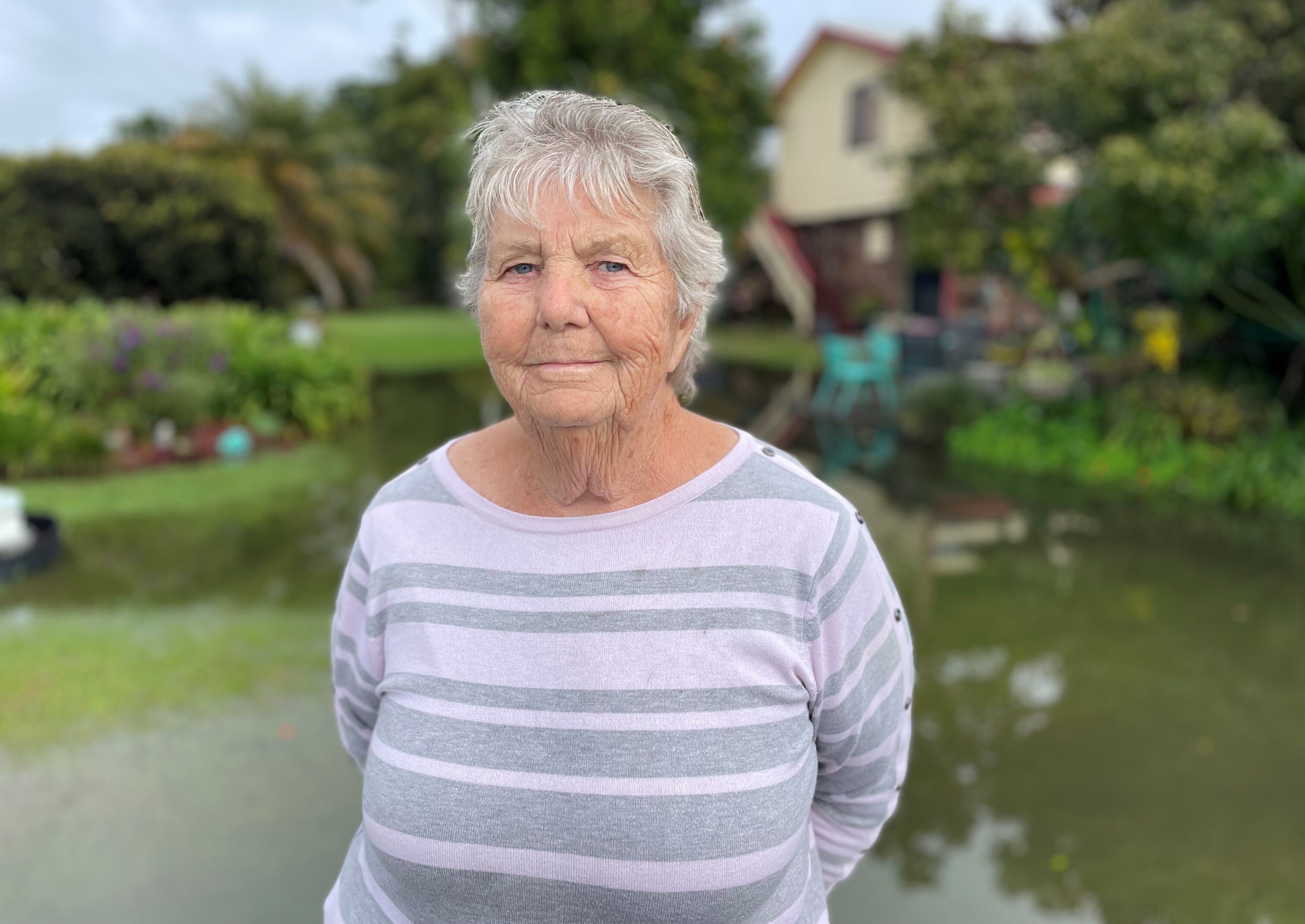 A woman stands in front of a flooded house yard