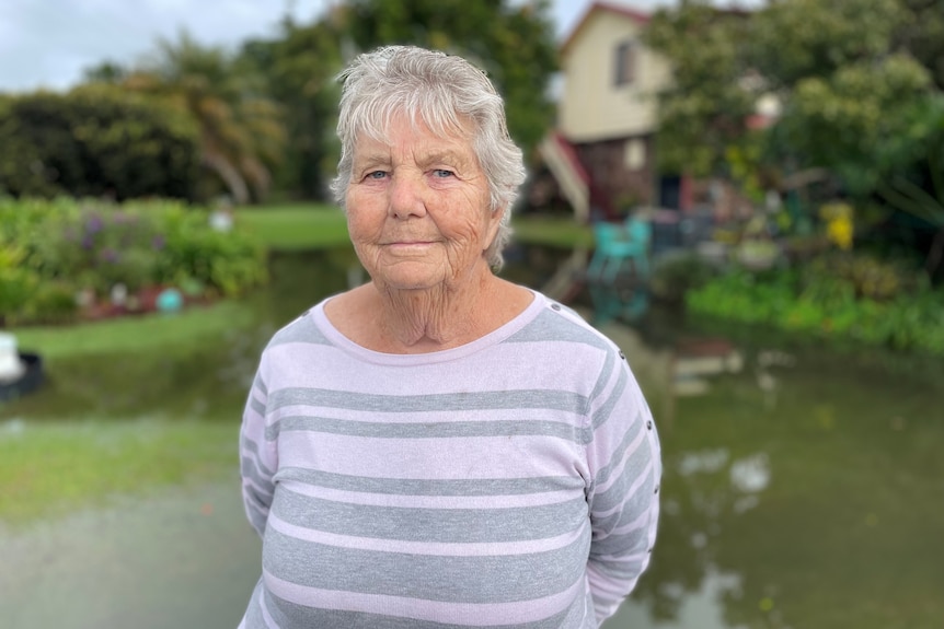 A woman stands in front of a flooded house yard