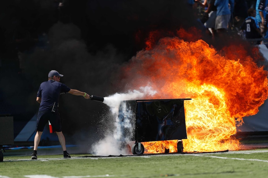 A man tries to put out a large fire inside a football stadium