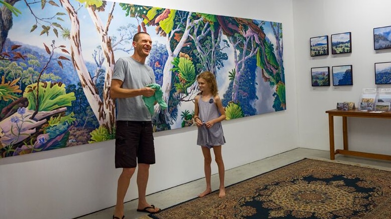 Man stands with daughter in front of a large landscape painting of a rainforest