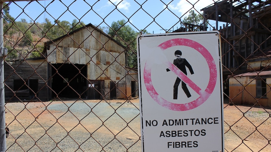 very old buildings behind wire fencing with a sign about absestos