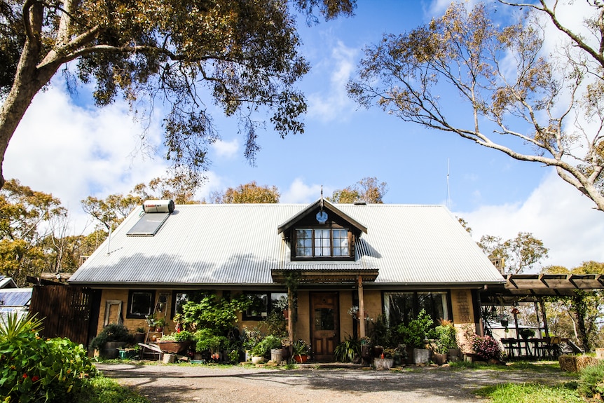 A rustic-looking house surrounded by green plants with solar hot water system on the roof.