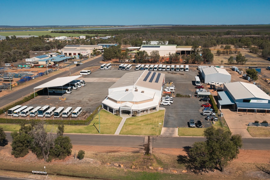 A drone shot of land, with a couple large sheds and buses lined up.