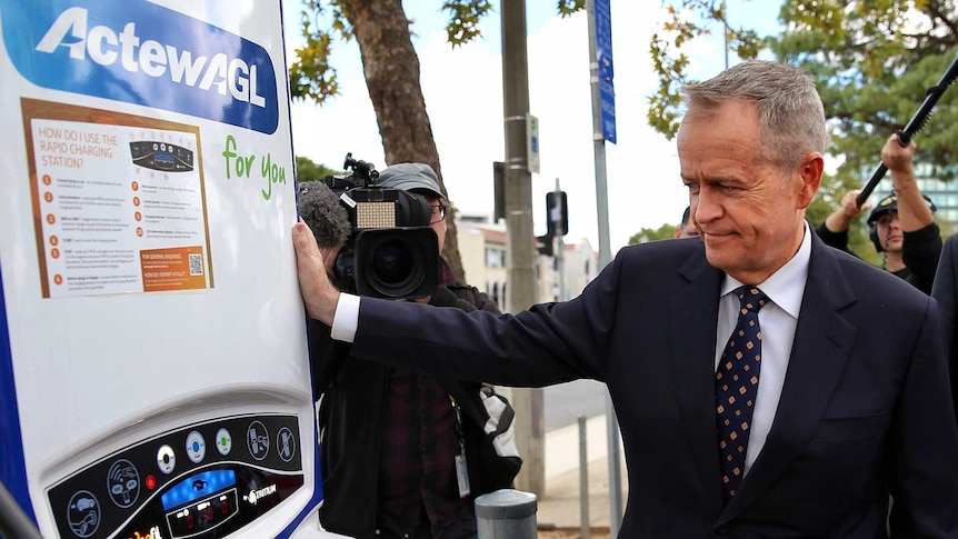 Bill shorten leans against a car recharge station as Anthony Albanese looks on