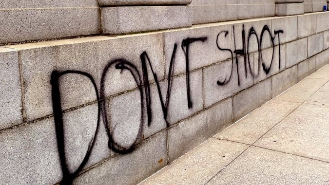 Black spray paint on the wall of a classical style public building in Indianapolis reading 'don't shoot'