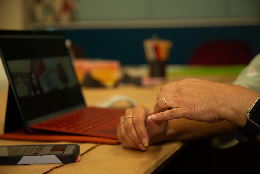 Close up of hands held together over a computer keyboard, which sits on a desk. Background is indoors and blurred.