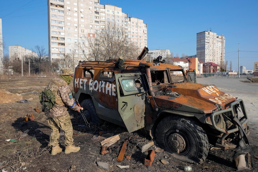 A Ukrainian soldier inspects a destroyed Russian APC vehicle.