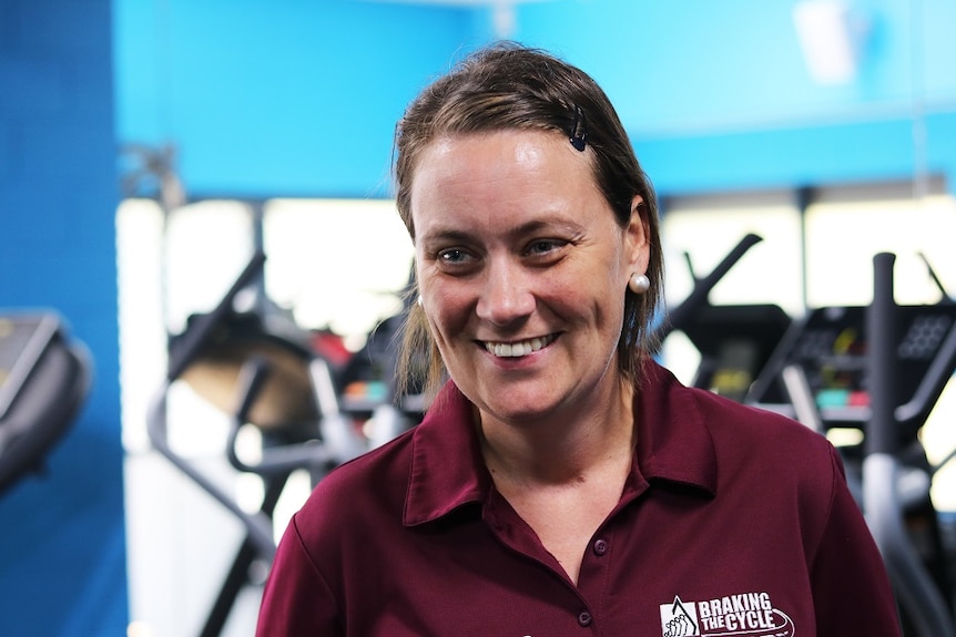 A woman standing in front of some treadmills smiles at the camera.